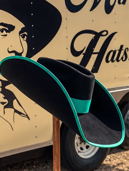 A black western hat with steeply lifted brim edges, teal edge binding and a matching teal band