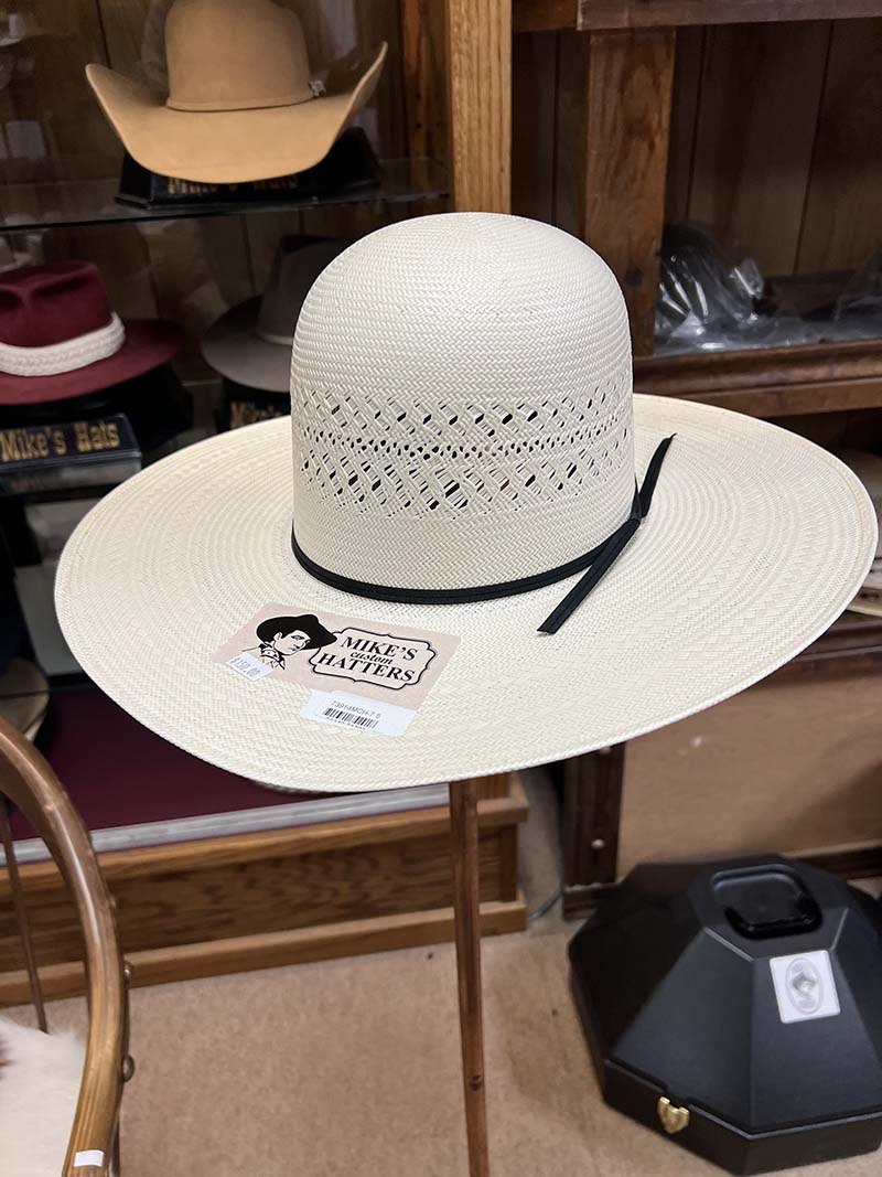 A white straw western hat with a black band on a stand in Mike’s shop