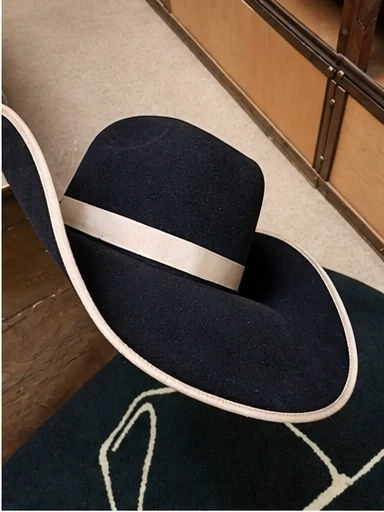 A dark western hat with lifted brim edges, pale edge binding and a light hatband