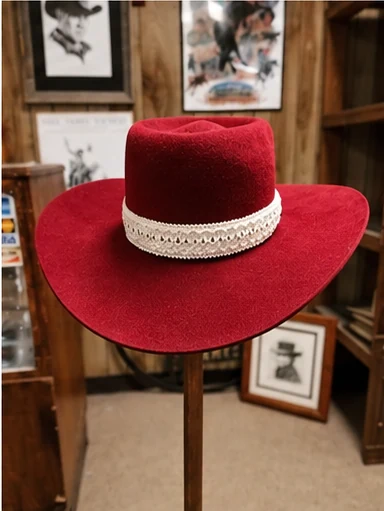 A rich red hat with a broad brim and a pale decorative patterned band on a stand