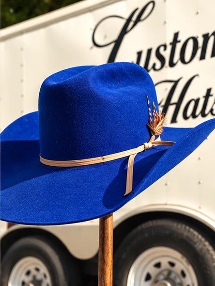 A royal-blue hat with a broad brim, tan tie band and feather accent