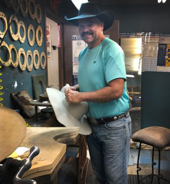 A hatmaker holding a western hat inside Mike’s actual Longview workshop