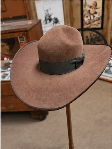 A warm taupe hat with a broad brim, dark ribbon band and fine dark edging on a stand